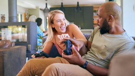 Couple On Sofa At Home Together Playing Computer Game With Multi-Generation Family In Background