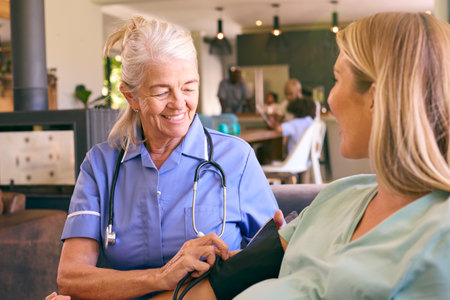 Senior Midwife Visiting Pregnant Woman At Home Taking Blood Pressure With Family In Backgroundの写真素材