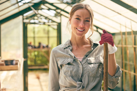 Portrait Of Smiling Woman With Broom Working In Greenhouse At Homeの写真素材