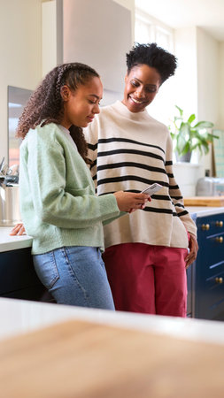 Mother Talking With Teenage Daughter At Home As She Checks Social Media On Mobile Phoneの写真素材
