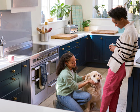 Mother Talking With Teenage Daughter Relaxing At Home In Kitchen With Pet Dogの写真素材