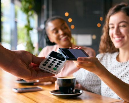 Woman In Coffee Shop Paying Bill With Contactless Mobile Phone Paymentの写真素材