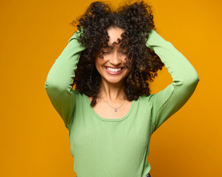 Studio Portrait Of Smiling Woman Standing Against Yellow Background Holding Up Hairの写真素材