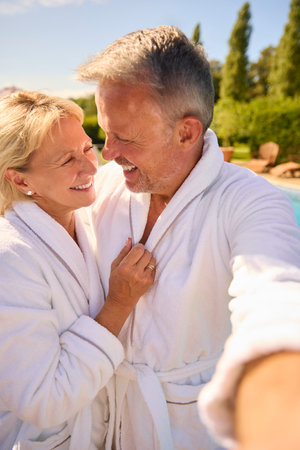 POV Shot Of Senior Couple In Robes Outdoors By Swimming Pool On Spa Dayの写真素材