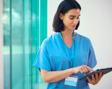 Mature Female Doctor Wearing Scrubs Using Digital Tablet In Hospitalの写真素材