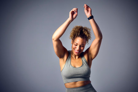 Studio Shot Of Woman Wearing Gym Fitness Clothing Dancing In Class On Grey Background