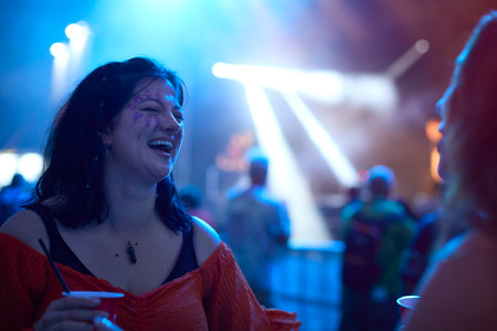 Two Female Friends Wearing Glitter Dancing At Outdoor Summer Music Festival Holding Drinks At Night