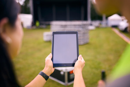 Close Up Of Production Team Looking At Digital Tablet Setting Up Outdoor Stage For Music Festivalの写真素材