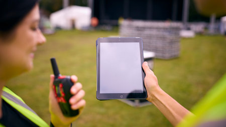 Close Up Of Production Team Looking At Digital Tablet Setting Up Outdoor Stage For Music Festival