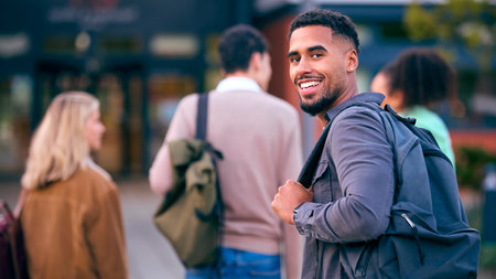 Portrait Of Male University Student Looking Over Shoulder With Friends Outside College Buildings