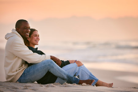 Casually Dressed Loving Young Couple Sitting On Beach Shoreline Hugging At Sunriseの写真素材