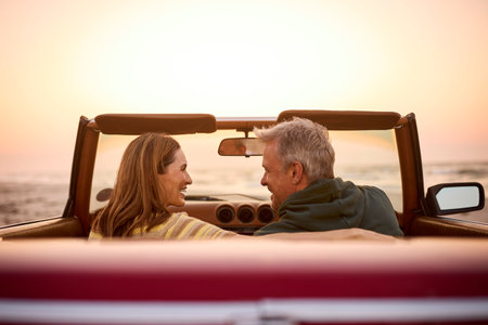 Rear View Of Retired Senior Couple On Vacation In Classic Sports Car At Beach Watching Sunriseの写真素材