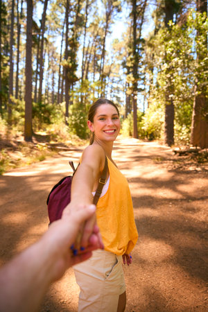 POV Shot Of Loving Couple Wearing Backpacks Holding Hands Hiking Along Trail Through Countrysideの写真素材