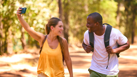 Couple Hiking Along Trail In Countryside Posing For Selfie Or Filming Video On Mobile Phoneの写真素材