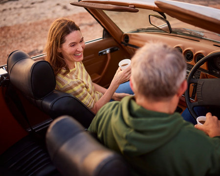 Retired Senior Couple In Classic Sports Car With Hot Drink At Beach Watching Sunriseの写真素材