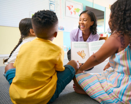 Female Primary Or Elementary School Teacher Reads Story To Multi-Cultural Class Seated In Classroomの写真素材