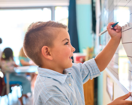 Male Primary Or Elementary School Student Writing On Whiteboard In Classroom Lesson