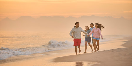 Couple With Friends On Vacation Holding Hands Running Along Beach Shoreline At Dawnの写真素材