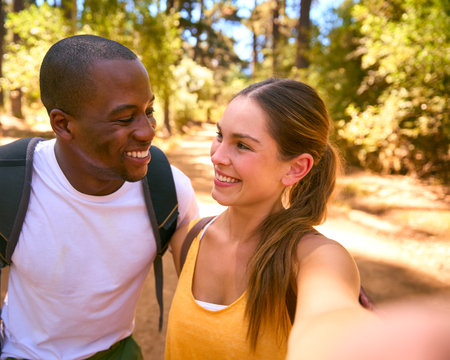 POV Shot Of Couple Hiking Along Trail Through Countryside Posing For Selfie On Mobile Phoneの写真素材