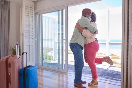 Loving Mature Couple With Luggage Arriving In Beachfront House Overlooking Ocean For Summer Vacationの写真素材