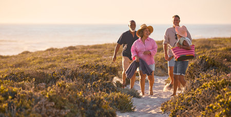 Mature Couple With Friends On Summer Vacation Walking Through Dunes On Way To Beach Carrying Bagsの写真素材