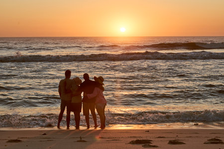 Rear View Silhouette Of Mature Couple With Friends On Beach Looking Out To Sea At Sunsetの写真素材