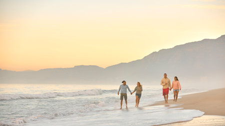 Couple With Friends On Vacation Holding Hands Walking Along Beach Shoreline At Dawnの写真素材