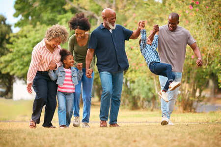 Three Generation Family Walking Outdoors Laughing And Playing And Swinging Grandchildren Between Themの写真素材