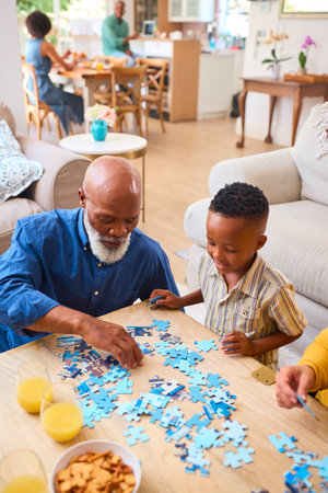 Grandparents With Grandchildren Indoors At Home Doing Jigsaw Puzzle With Parents In Background