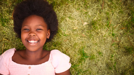 Looking Down On Smiling And Laughing Young Girl Outdoors Lying On Grass In Garden Or Countrysideの写真素材