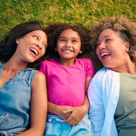 Looking Down On Three Generation Female Family Laughing And Lying On Grass Outdoors In Countryside