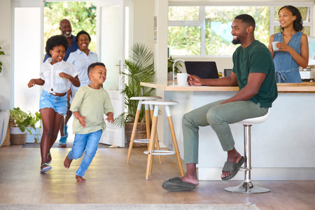 Grandparents With Grandchildren Returning Home To Parents Working On Laptop In Kitchen