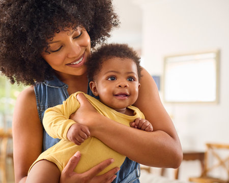 Loving Mother Indoors At Home Standing Cuddling Baby Daughter