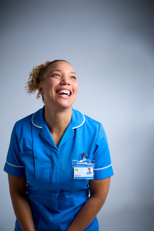 Studio Portrait Of Smiling Female Nurse Wearing Uniform With Digital Tablet Against Grey Backgroundの写真素材