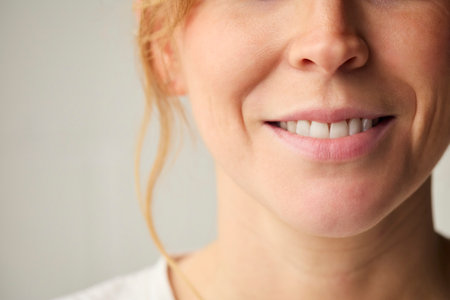 Studio Shot Of Woman Smiling Against Plain Background With Close Up On Lips And Teeth