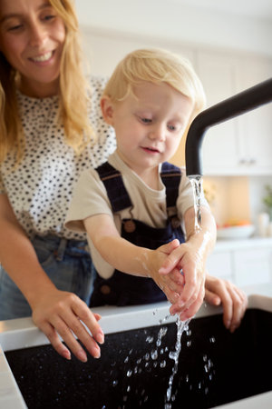 Mother With Son At Home In Kitchen Washing Hands In Sink Or Basin Together With Focus On Foregroundの写真素材