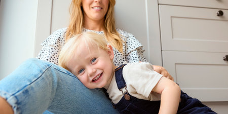 Portrait Of Young Son Playing Game With Mother Sitting On Floor At Home In Kitchen Togetherの写真素材