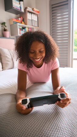 Teenage Girl Lying On Bed At Home Playing With Handheld Gaming Device