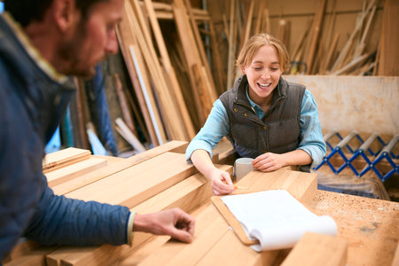 Male And Female Carpenter Working In Woodwork Workshop Discussing Plan Together