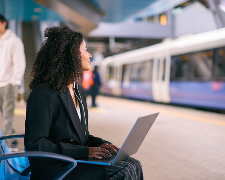 Businesswoman Commuting On Train Platform Working On Laptop Wearing Earphonesの写真素材