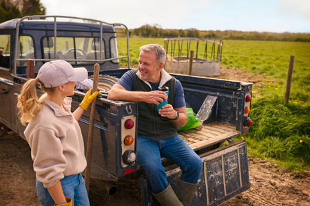 Mature Male Farm Worker Sitting On Tailgate Of Off Road Farm Vehicle Talking With Female Colleague