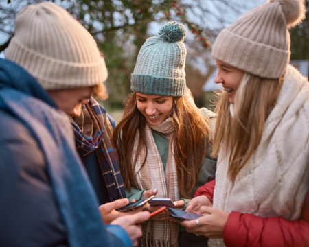 Group Of Teenage Girls And Boys Outdoors Dressed For Winter All Holding Mobile Phones