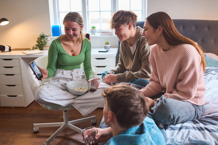 Group Of Teenage Friends At Home In Bedroom Looking At Social Media On Mobile Phone