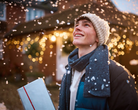 Smiling Teenage Boy Outdoors Dressed For Winter In Snow Delivering Christmas Presentsの写真素材