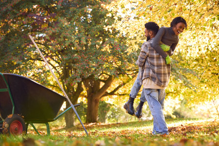 Young Couple With Man Lifting Up Woman As They Collect Autumn Leaves In Gardenの写真素材