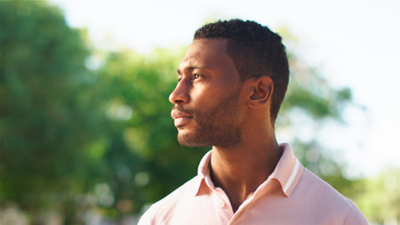 A young man stands outdoors, enjoying a moment of reflection as he looks towards the horizon....