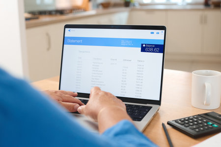 A person is intently focused on a laptop screen displaying a financial statement in a modern...
