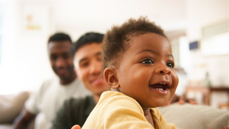 A joyful baby smiles while two adults look on from behind.