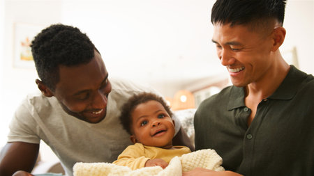 Two dads enjoy playful moments with their happy baby at home.