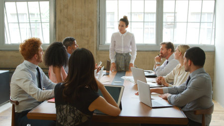 Young Businesswoman Giving Presentation To Multi-Cultural Team Sitting Around Table In Modern Officeの写真素材